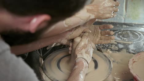 a potter teaches a woman to make clay dishes. a man takes a woman's hands