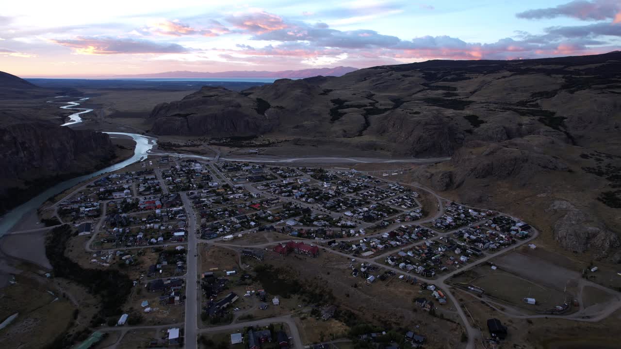 Aerial Drone Footage Captures El Chaltén Village In Argentina At Sunrise, Nestled In Shadowed Mountains. The Las Vueltas River Flows Nearby, Creating A Serene, Cold Summer Morning Atmosphere.