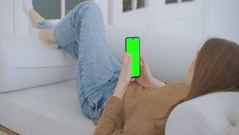 Woman-at-Home-Lying-on-a-Couch-using-Smartphone-with-Green-Mock-up-Screen-Doing-Swiping-Scrolling-Gestures.-Guy-Using-Mobile-Phone-Internet-Social-Networks-Browsing.-Point-of-View-Camera-Shot