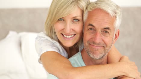 Couple-embracing-and-smiling-at-camera-in-bed-together