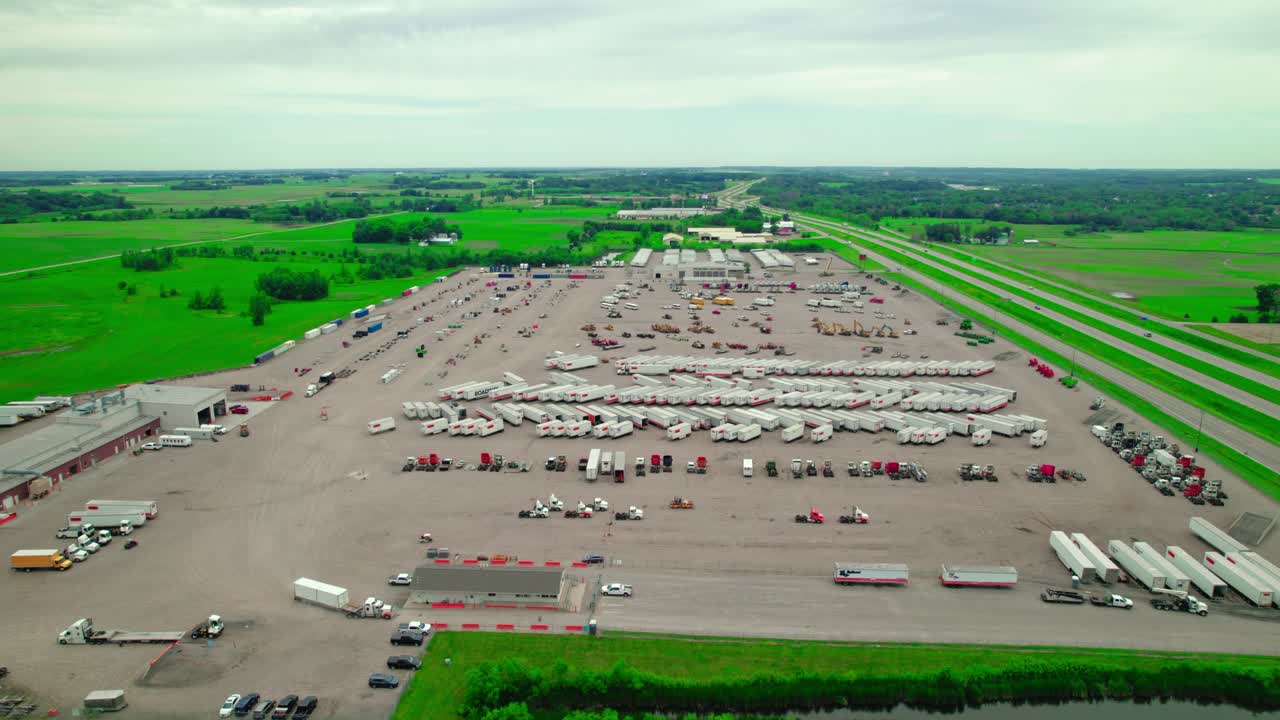 Aerial view of Ritchie Bros. Auctioneers facility featuring an expansive lot filled with various heavy equipment, trucks, and trailers, located next to a highway.