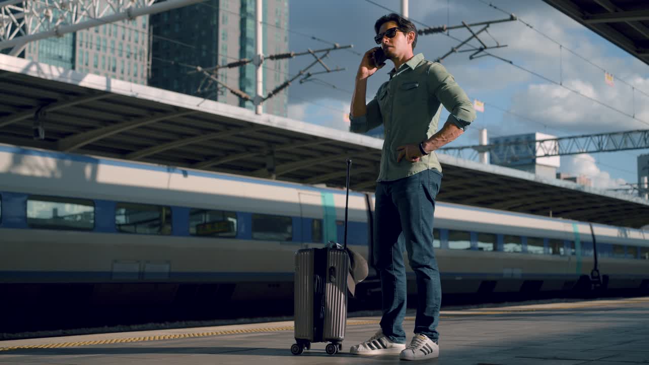 Man talking on phone while waiting for train at Seoul station, South Korea, stylish solo traveler with hard case luggage in the city