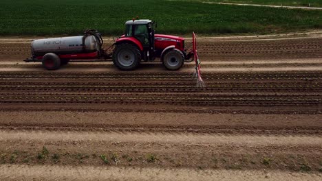 drone flight near tractor drives over field and pours young lettuce plants with water