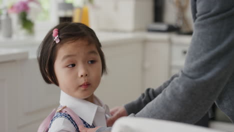 작은 아시아 소녀가 학교에 갈 준비를 하고 있습니다. 행복한 아버지가 딸을 첫날을 위해 준비하고 있습니다. 그녀의 머리에 키스를 해서 작별 인사를 하고 있습니다.
