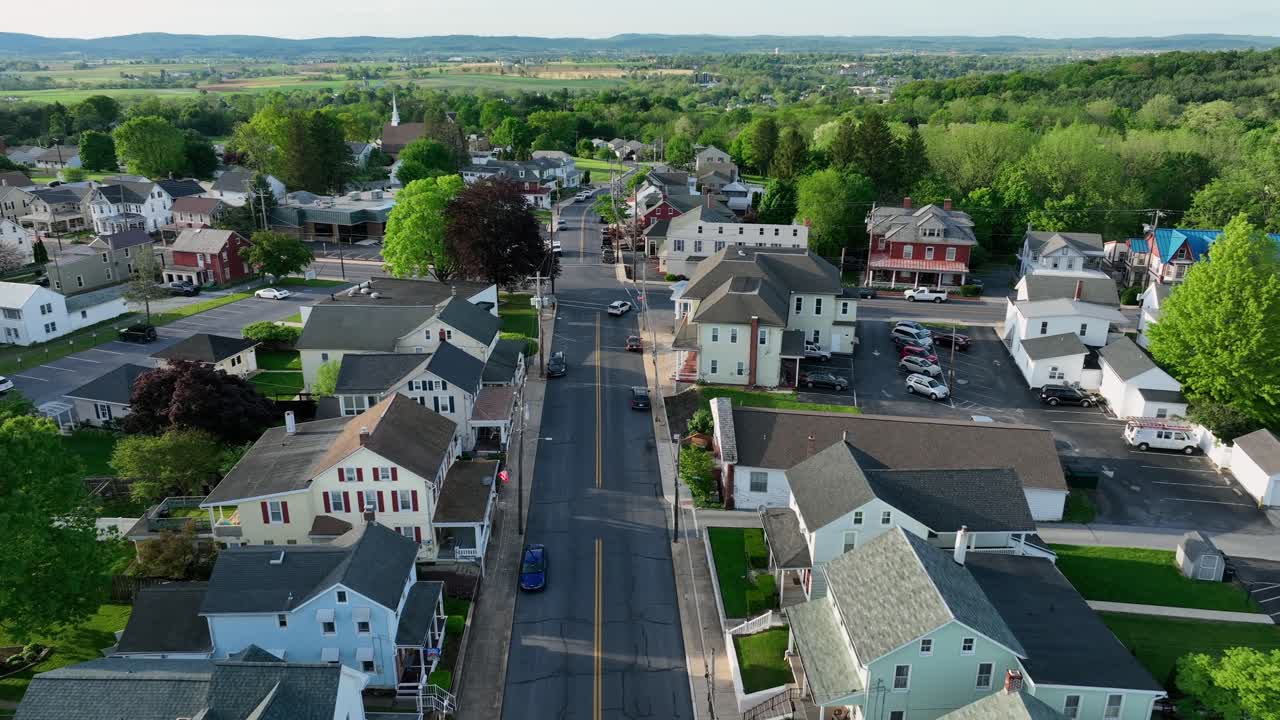 Aerial establishing shot of american small town with colorful houses and green trees in spring. Driving Cars on straight road at sunset. Drone Birds Eye. Wide shot. Akron, Lancaster, PA.