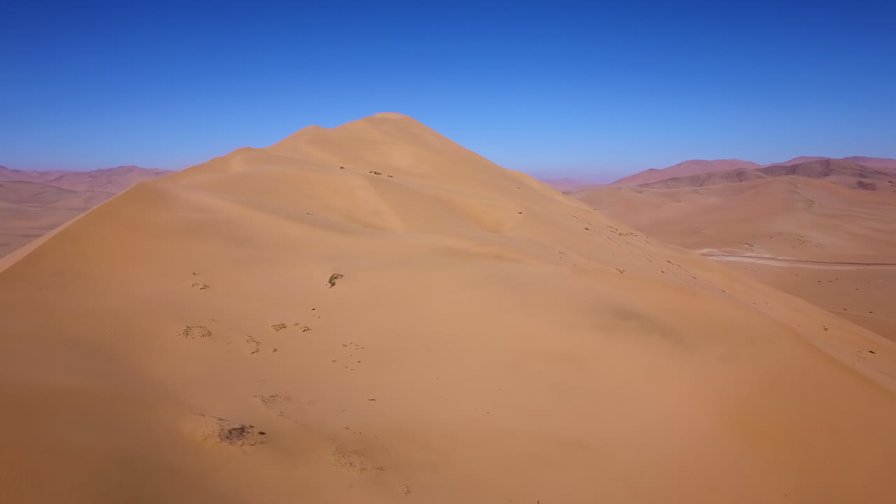 칠레 아타카마 사막의 공중 풍경, 수평선과 밝은 푸른 하늘을 드러내기 위해 큰 모래언덕 위로 솟아오른다