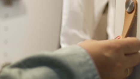 close-up of a woman's hand opening a cabinet door with a leather handle