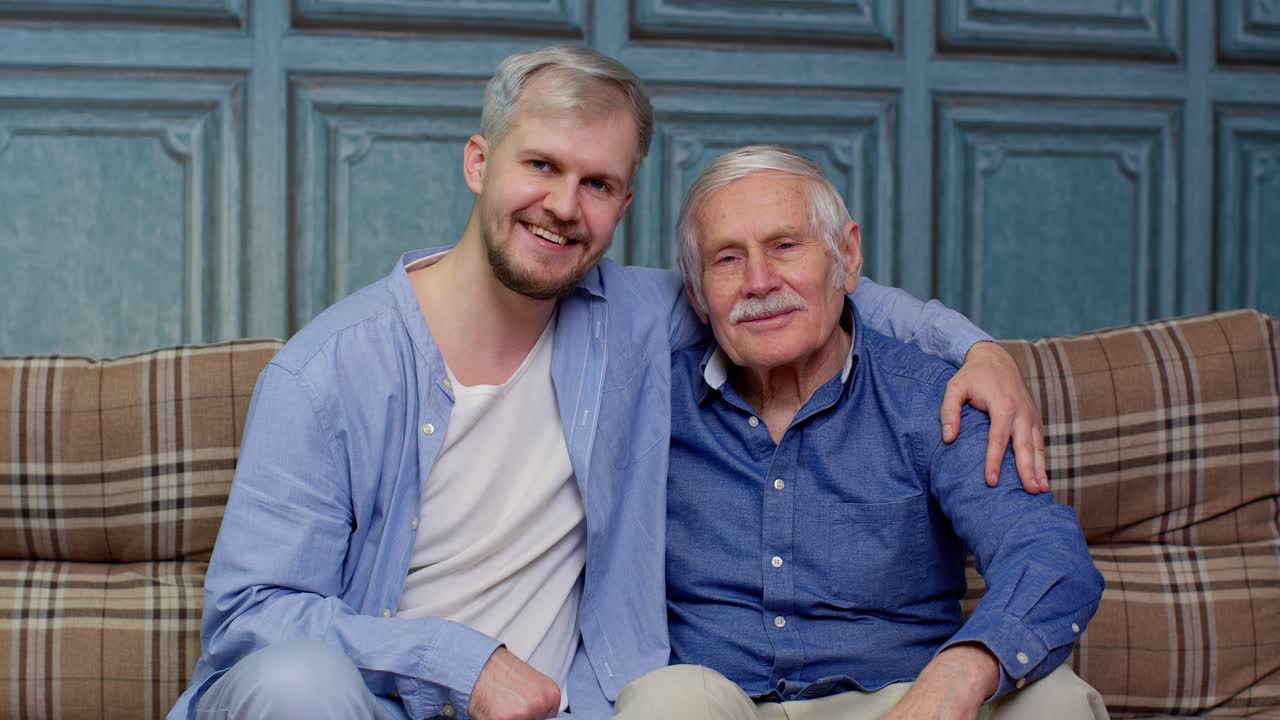 Ein Mann und sein Sohn sitzen zusammen auf einem Sofa und lächeln in die Kamera.