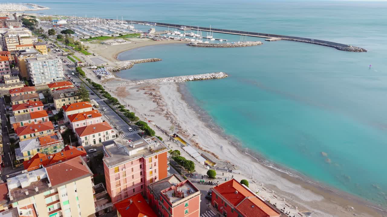 Coastal town with red rooftops, clear sea, marina and beach in Italy, aerial view