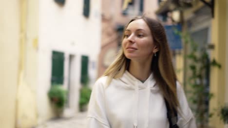 a woman walks along a city narrow street with backpack and smiling