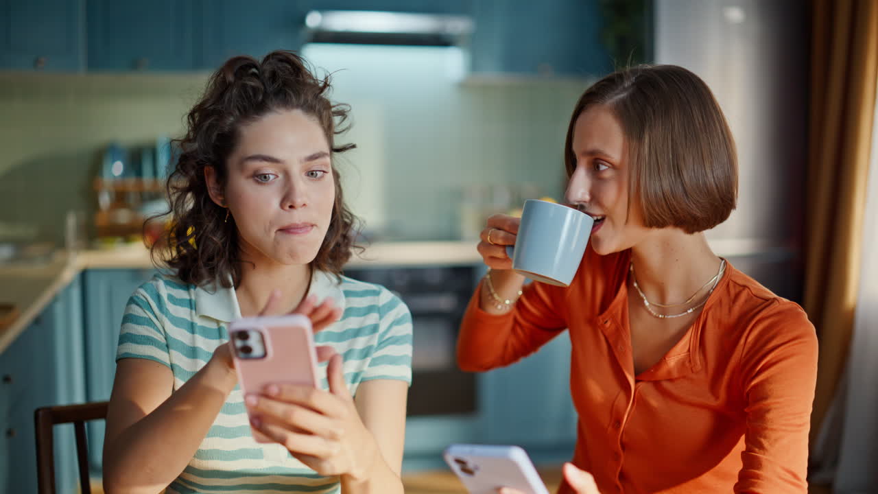 Usměvavé dívky diskutují o novinkách ze sociálních médií a drží chytré telefony, detailní záběr z domova