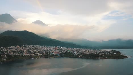 drone aerial view of a town and a beautiful rainbow in lake atitlan, guatemala - mountains and volcanoes landscape