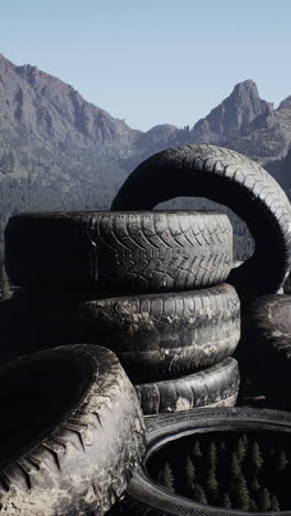 a stack of old, worn tires sits against a backdrop of mountains and forest.