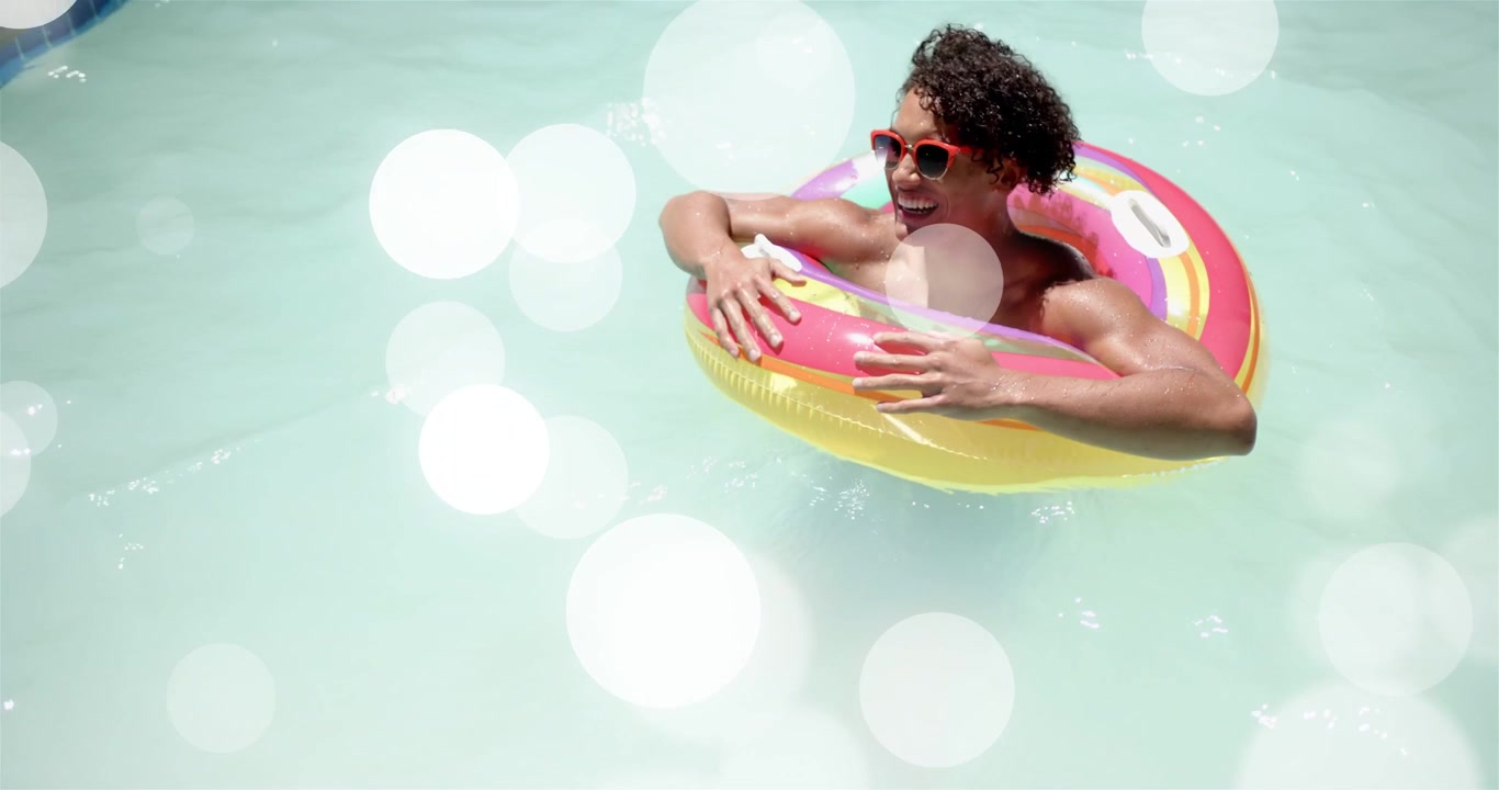 Man floating aqua pool in rainbow ring, sun making bokeh over him, laughing shifting grip marketing