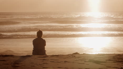 vista trasera de una mujer mayor en la playa viendo la puesta de sol sobre el océano