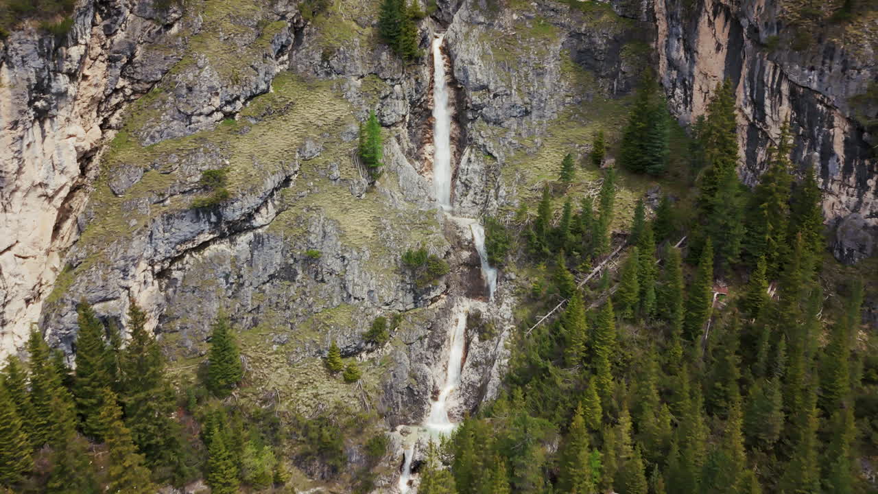 imágenes aéreas de una cascada vertical que cae en cascada por escarpados acantilados rocosos en los dolomitas, rodeada de bosque verde