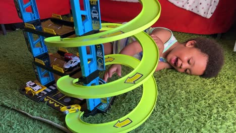 joyful 3-year-old black toddler playing with his new toy garage at home, lying on a green rug