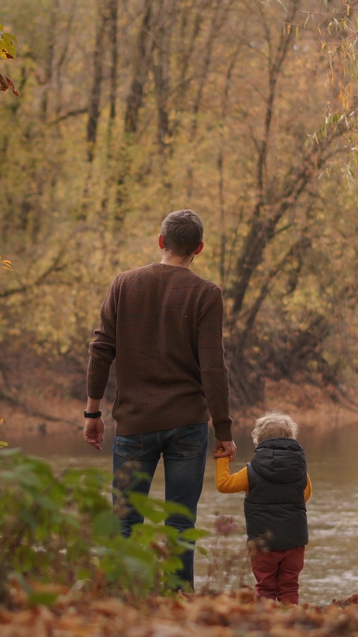 Padre e figlio in piedi insieme in riva a un fiume in autunno