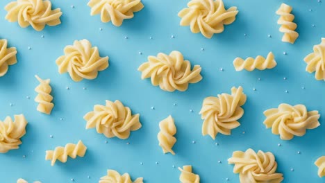 different pasta shapes, including spirals and rosettes, are artfully scattered across a vibrant blue surface, creating a visually appealing arrangement