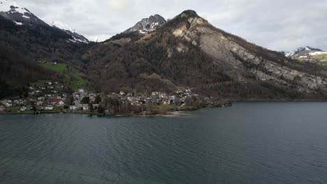 aerial static of windswept lake in switzerland with coastal community on shoreline below snowy mountains