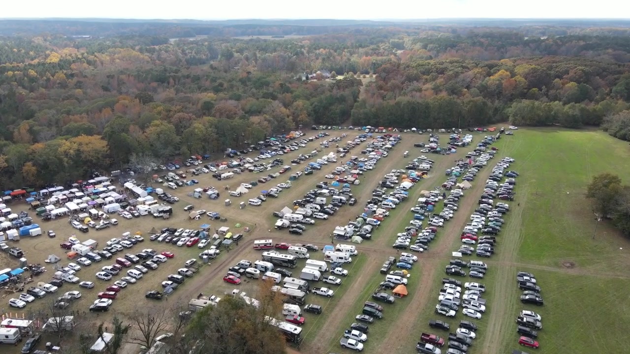 Survol d'un rassemblement en plein air avec des tentes et un parking.
