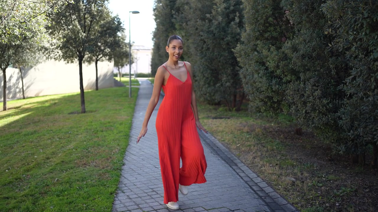 Una giovane donna in un abito rosso brillante si erge con grazia su un sentiero tra una vegetazione lussureggiante.