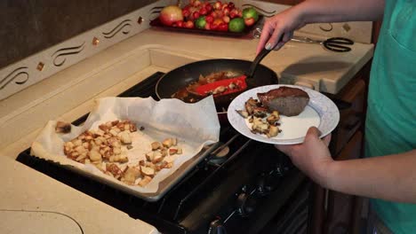 woman plating steak, grilled onions, sauteed miatake mushrooms and roasted potatoes in a small kitchen