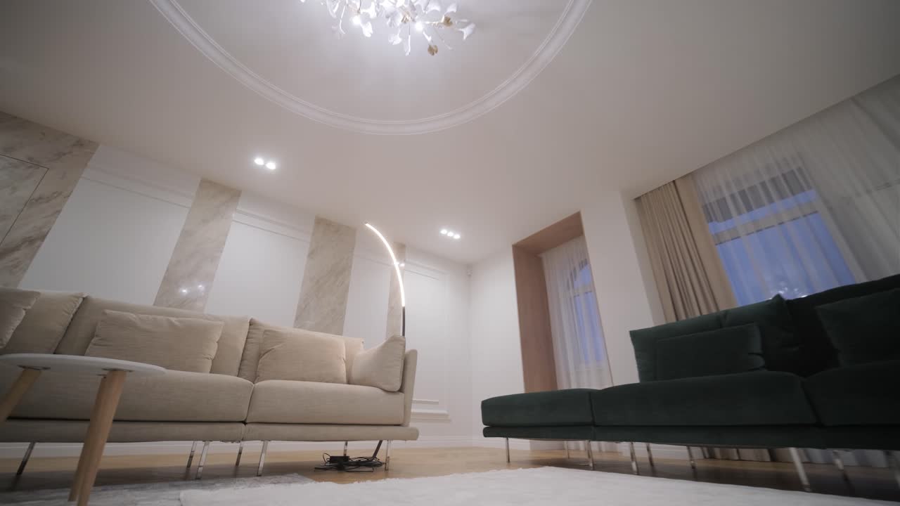 독특한 천장 조명 장치로 조명 된 정교한 거실, 우아한 베이지와 녹색 소파로 조용하고 고급스러운 분위기를 조성합니다.