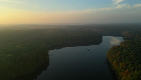 a serene lake surrounded by dense forests at sunrise with misty, golden light over calm water