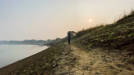 Man-jogging-towards-camera-on-walk-path-by-dry-river-bed-in-Sylhet,-pan