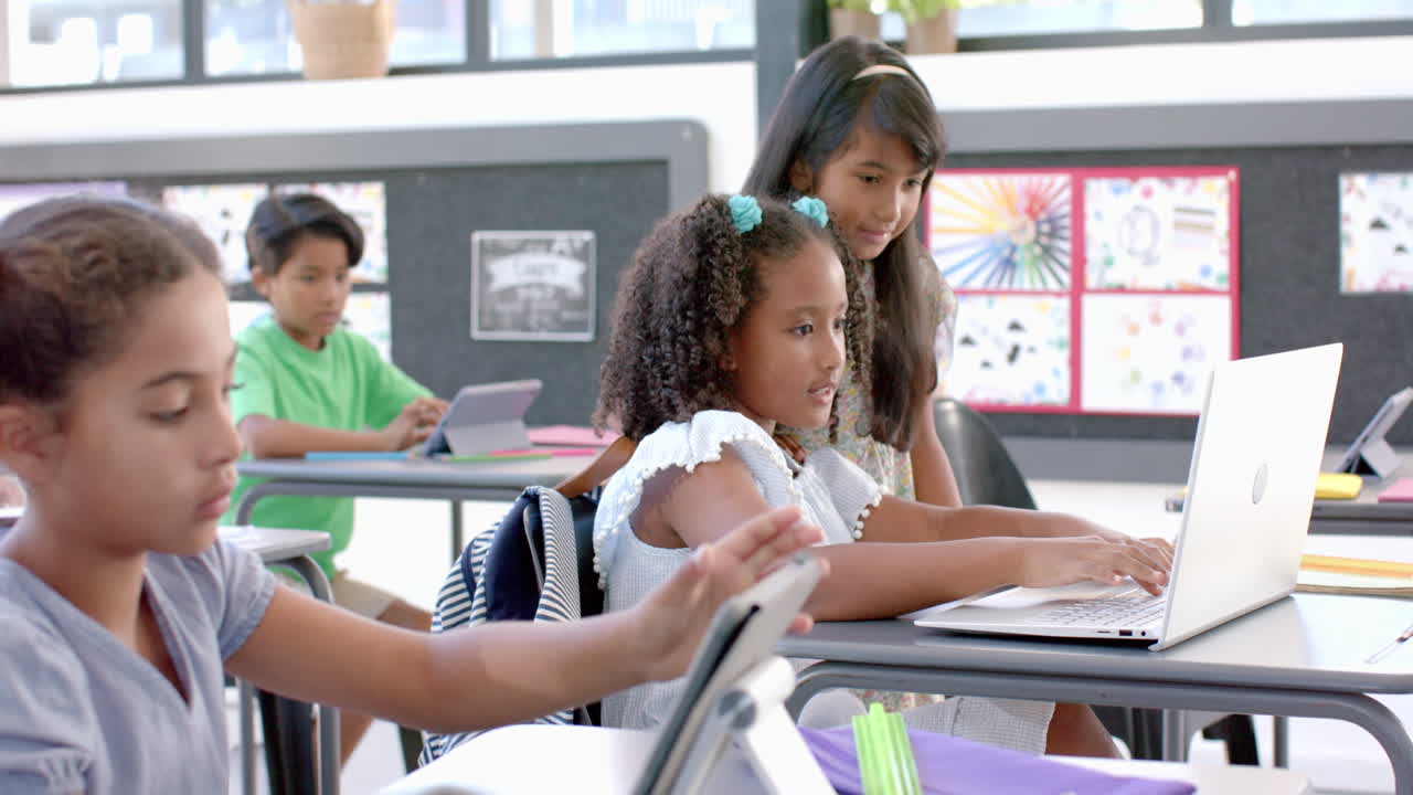 Biracial girls engage in a school project in a classroom with a laptop