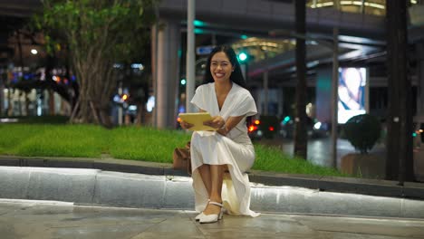 woman sitting on city street at night with a tablet