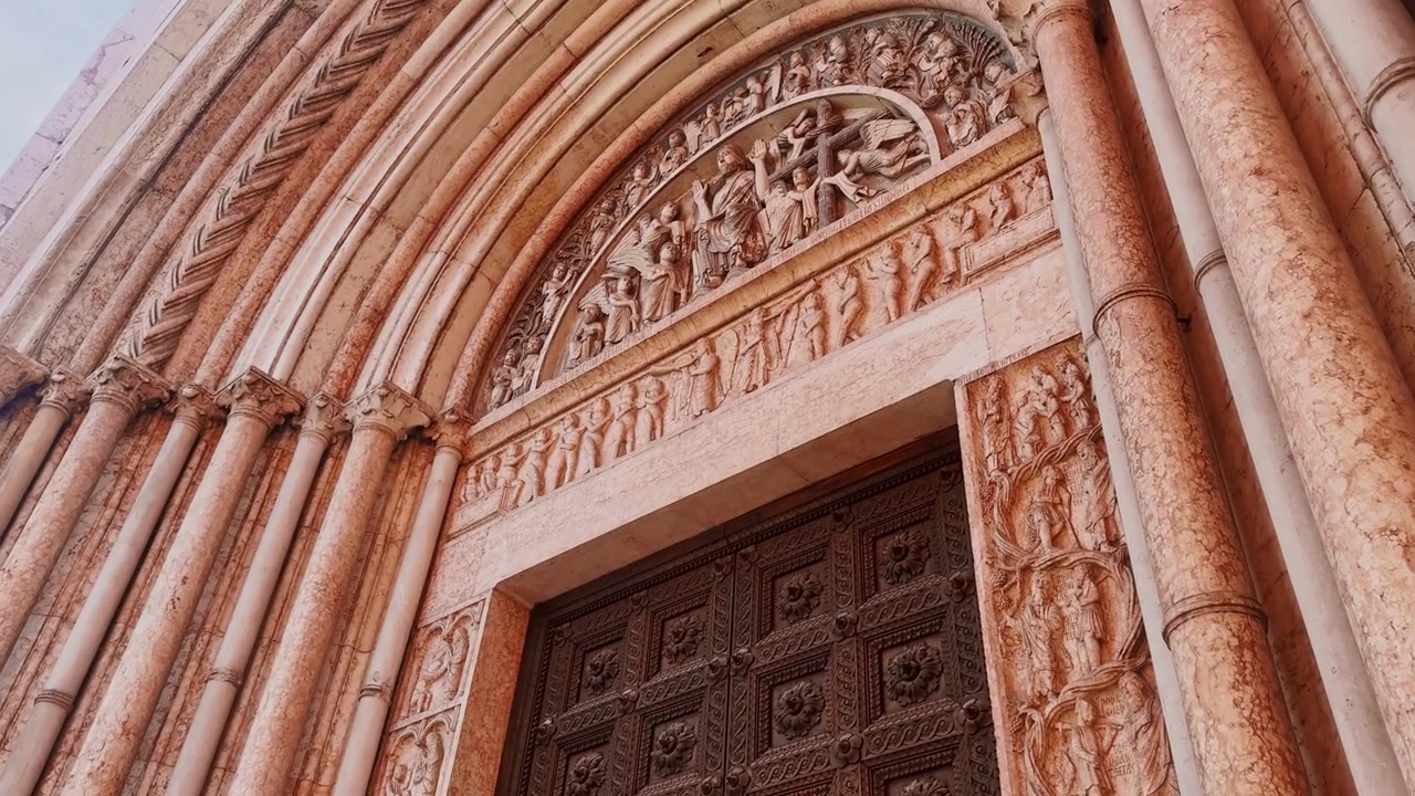 Primo piano del portale del Battistero di Parma, che mostra figure in marmo riccamente scolpite, colonne slanciate e un'ornata porta in legno medievale a Parma, Italia
