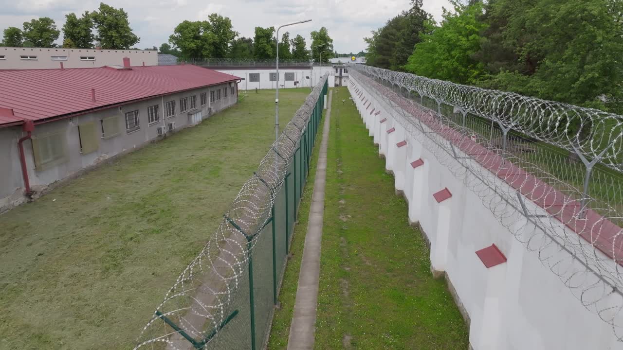 Aerial pull-out shot showing extensive concrete wall and barbed wire fence surrounding prison