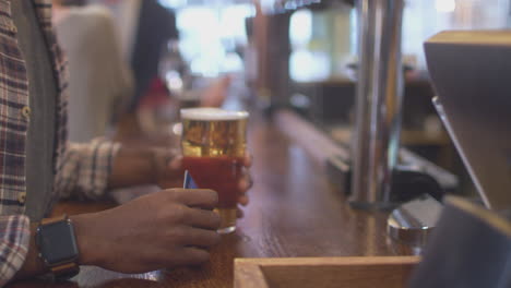 close up of male customer in bar making contactless payment for drinks in health pandemic