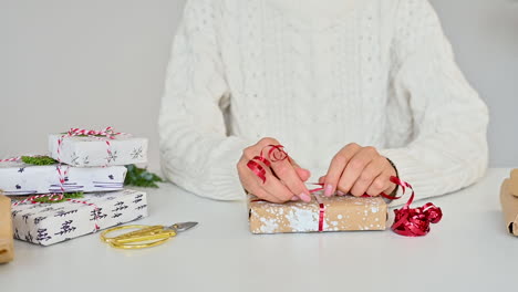 female hands tie the bow of a gift box with wrapping decorated with painted snow