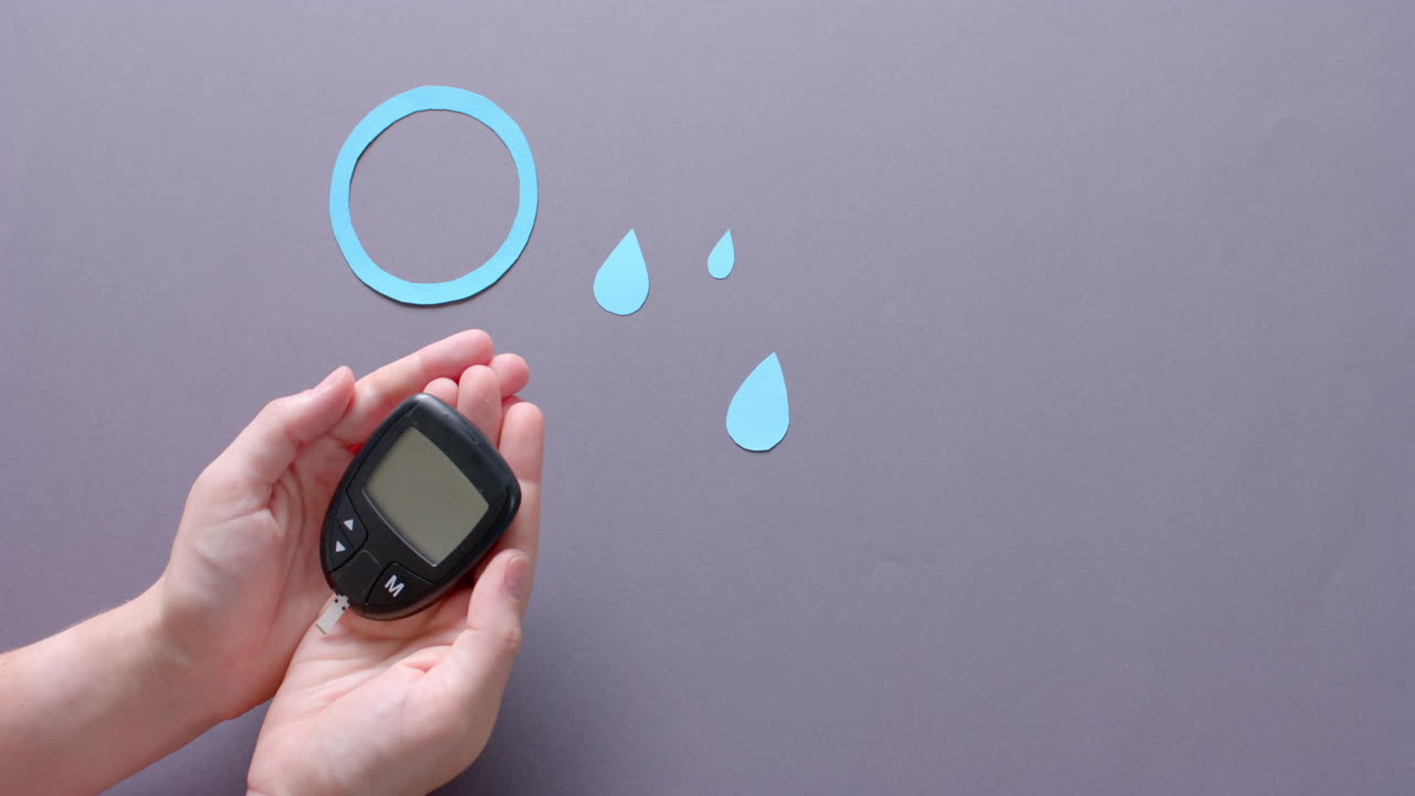 Hands of caucasian woman holding glucometer over blue drops and circle on grey, slow motion
