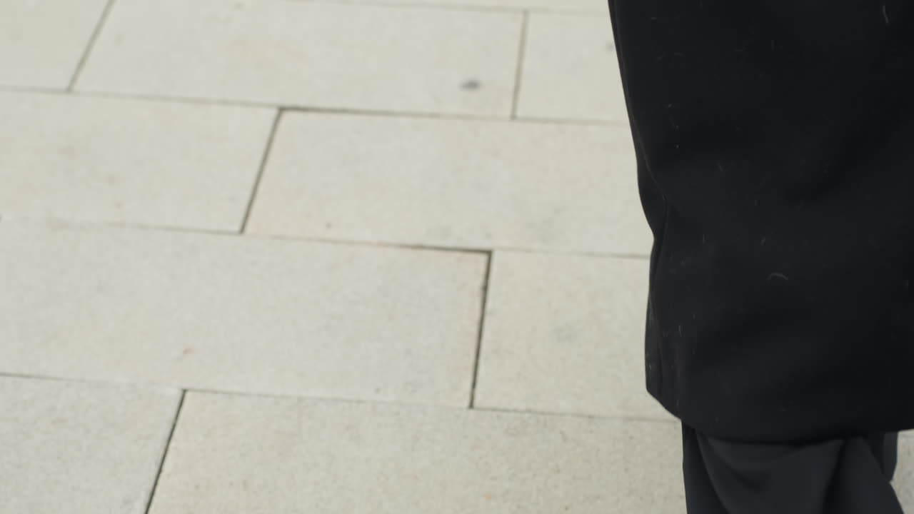 student walking on tiled pavement with denim backpack, brisk determined stride, black trousers and scuffed shoes, closeup of feet and steps, urban campus commute, textured concrete tiles, minimalist