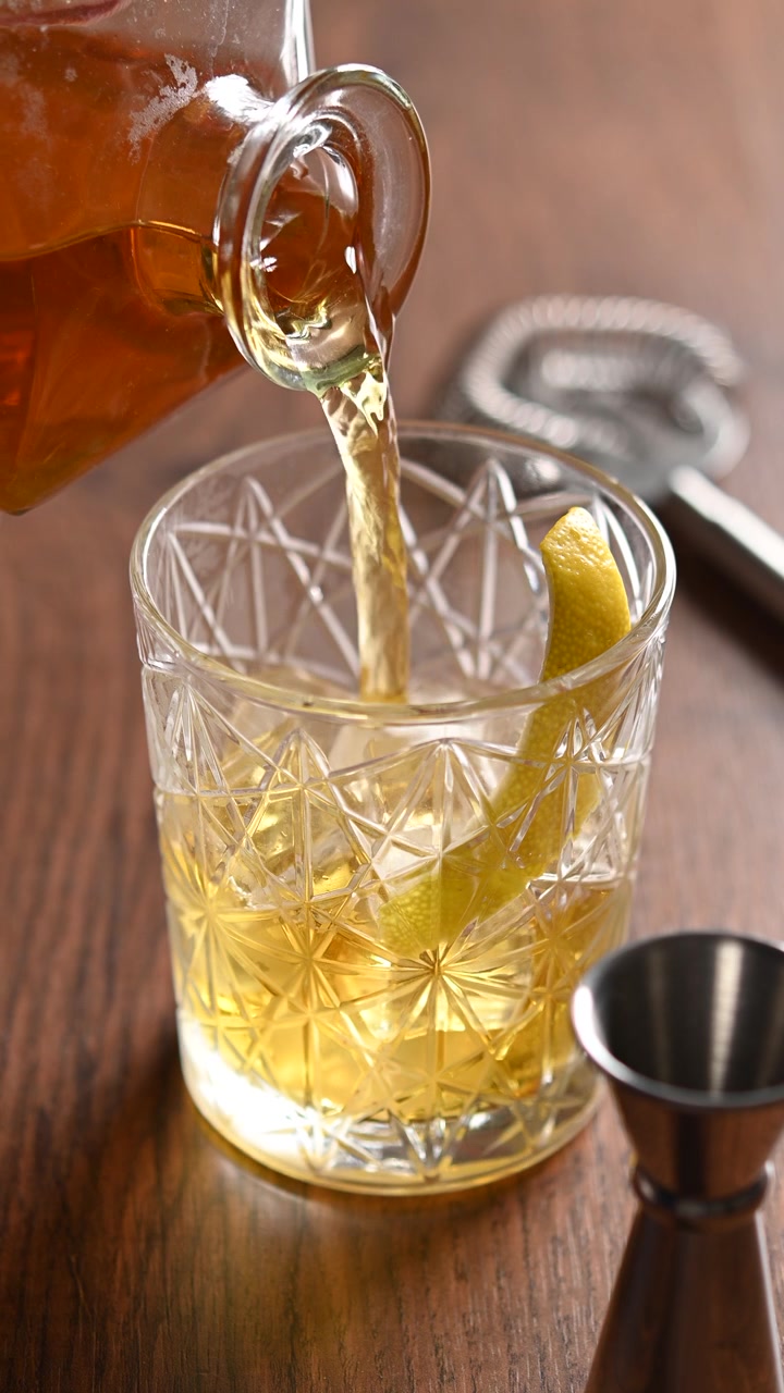 Cocktail Rusty Nail in rotazione in un bicchiere old fashioned con ghiaccio, primo piano di una bevanda ambrata.