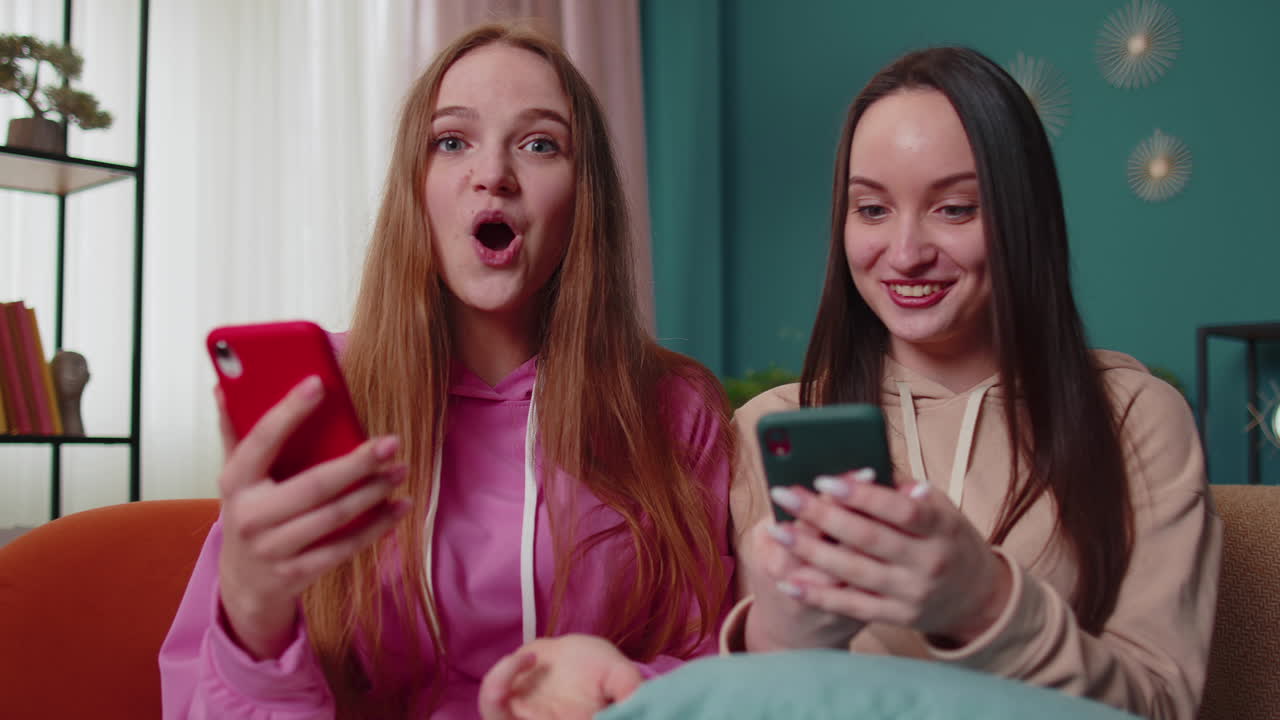Amiche e sorelle festeggiano il successo e la vittoria, esultano urlando, facendo shopping online sullo smartphone