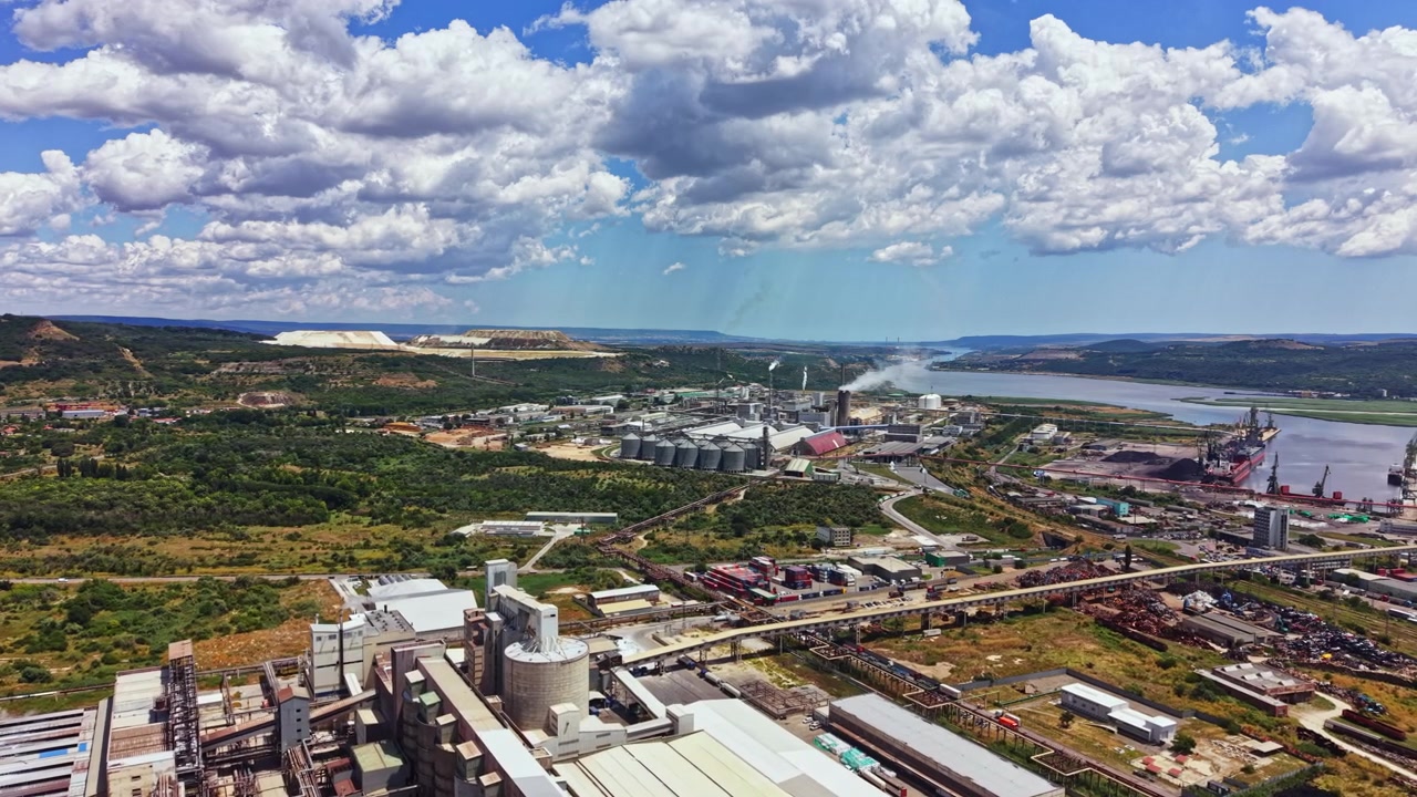 Zona industrial con fábricas y un río cerca de un paisaje durante el día con nubes en el cielo.