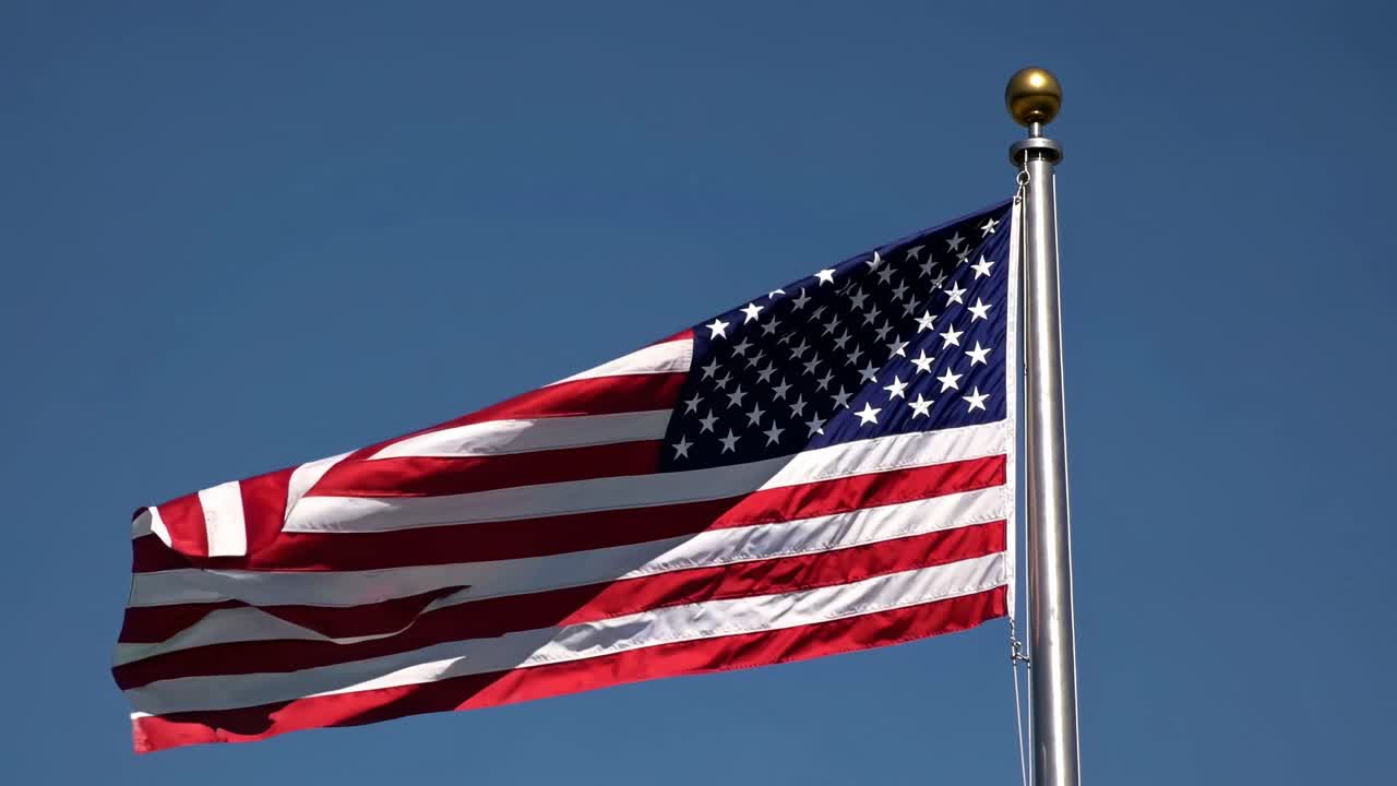 Video da angolazione bassa della bandiera americana che sventola contro un cielo azzurro limpido, enfatizzando il patriottismo