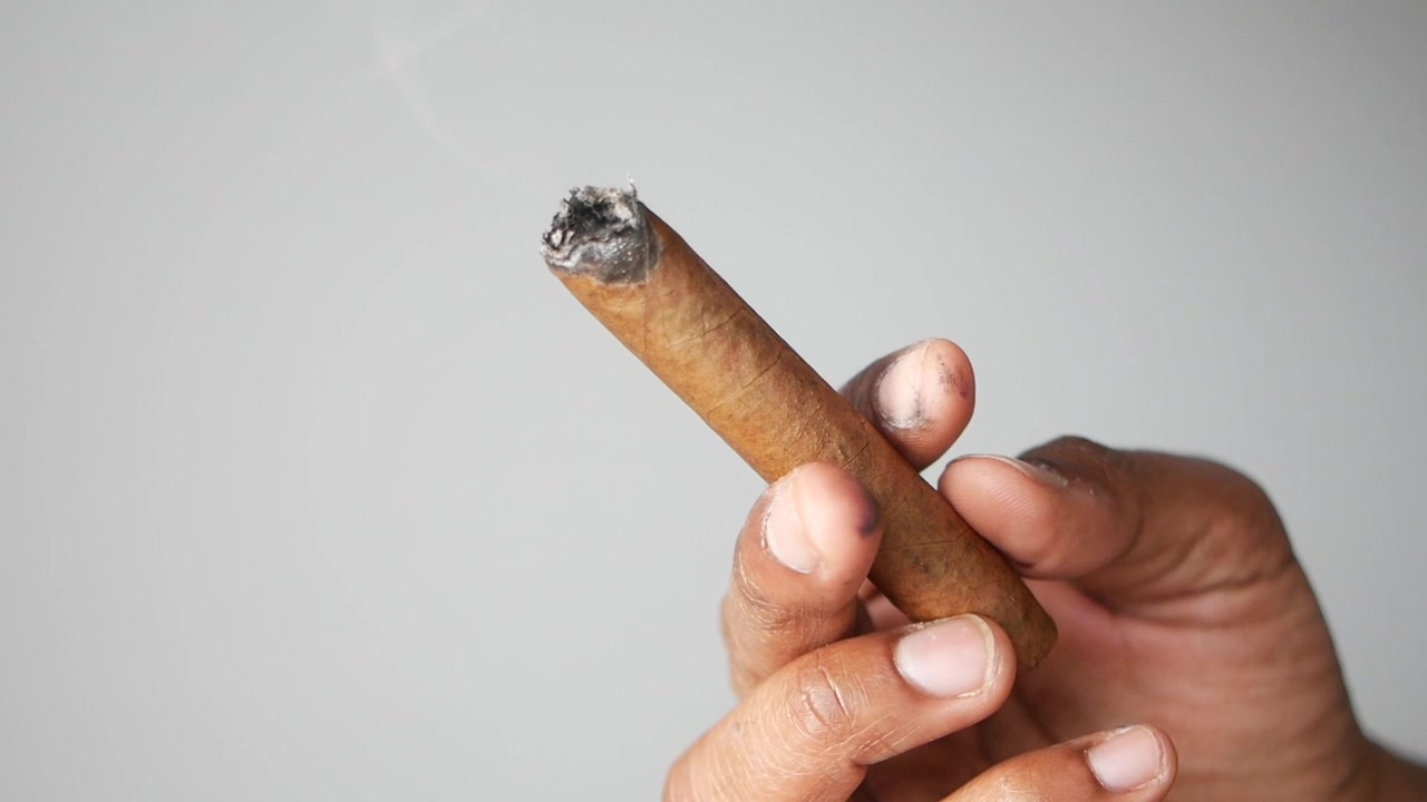 Primo piano di mano che tiene un sigaro acceso con fumo che sale