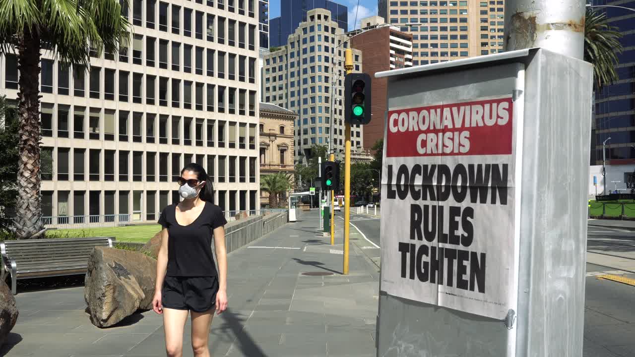 마스크를 쓴 여성이 코로나 바이러스 발생 시 신문 경고 옆으로 걸어갑니다.