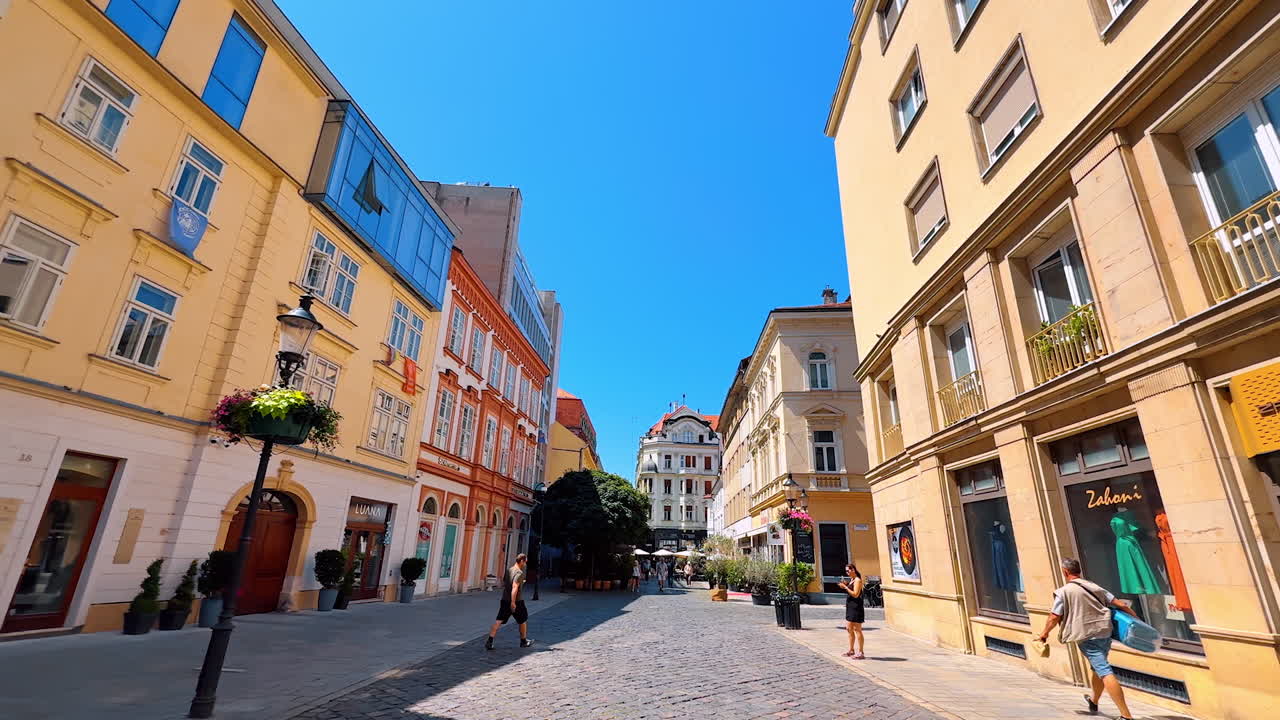 Few people walk by the paved road along the beautiful buildings. Walking by the old town of Bratislava, Slovakia