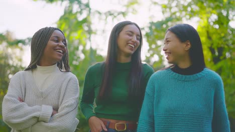 three diverse young women laughing and talking outdoors in a park
