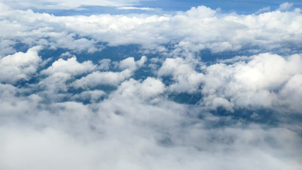 4K. aerial view through an airplane window. beautiful white clouds in blue sky background. traveling by air.