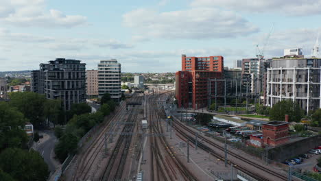 Forwards-tracking-of-train-slowly-driving-on-track-leading-around-modern-residential-buildings-in-city.-London,-UK