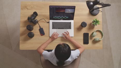 top view of a woman editor shaking her head and having a headache while sitting in the workspace using a laptop next to the camera editing the video at home