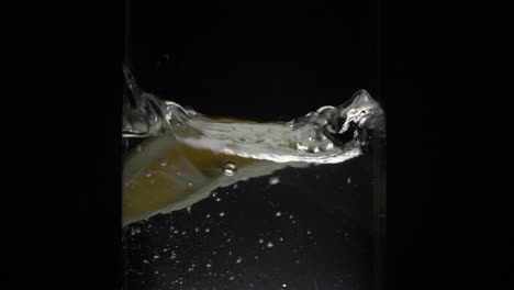 fresh slice of lemon falling into a glass of water with black background - wide shot, 180fps, slow motion